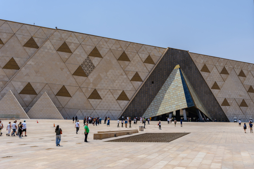 Giza Egypt 16 May 2026 View of the Grand Egyptian Museum with its modern triangular facade and people walking in the foreground under a clear blue sky.