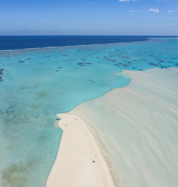 Aerial view of the pristine white sandbar surrounded by turquoise lagoon waters and coral reefs under a clear blue sky in Aitutaki Cook Islands. Aerial view of the pristine white sandbar surrounded by turquoise lagoon waters and coral reefs under a clear blue sky in Aitutaki Cook Islands.