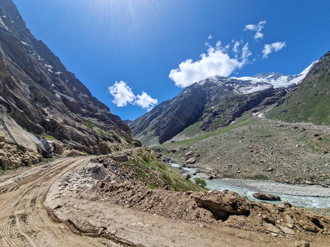 View of the rugged Penzi La road winding through the mountainous landscape with a glacial river and snow capped peaks under a clear blue sky in Zanskar Ladakh India.