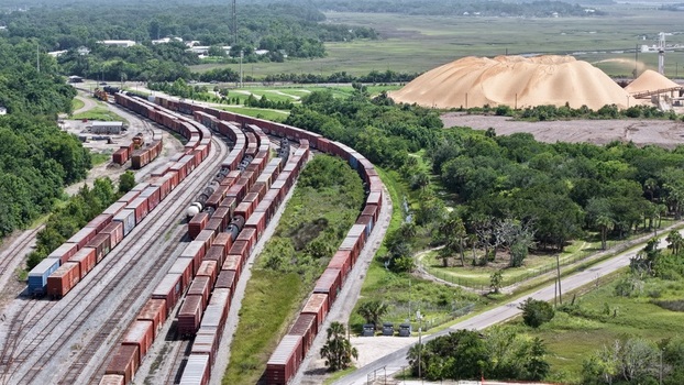 Aerial view of rows of freight trains snake through green trees contrasting with the immense golden piles of phosphate Fernandina Beach Florida United States. Aerial view of rows of freight trains snake through green trees contrasting with the immense golden piles of phosphate Fernandina Beach Florida United States.