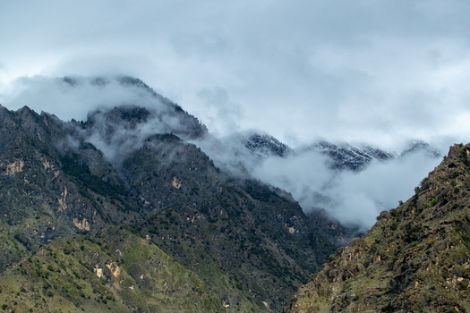 View of rugged mountain peaks partially shrouded in thick white clouds and mist with sparse vegetation on rocky slopes Chilas Gilgit Pakistan. View of rugged mountain peaks partially shrouded in thick white clouds and mist with sparse vegetation on rocky slopes Chilas Gilgit Pakistan.