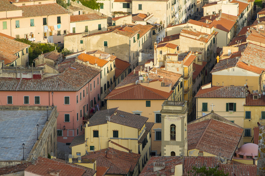 View of sun kissed terracotta roofs cascade down the hillside interspersed with pastel buildings creating a warm inviting urban landscape Portoferraio Elba Tuscany Italy. View of sun kissed terracotta roofs cascade down the hillside interspersed with pastel buildings creating a warm inviting urban landscape Portoferraio Elba Tuscany Italy.