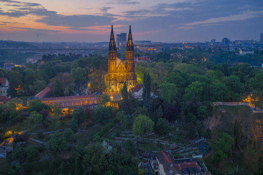 Aerial view of the illuminated Basilica of St Peter and St Paul at Vysehrad surrounded by lush greenery and historic fortifications during twilight in Prague Prague Czechia.
