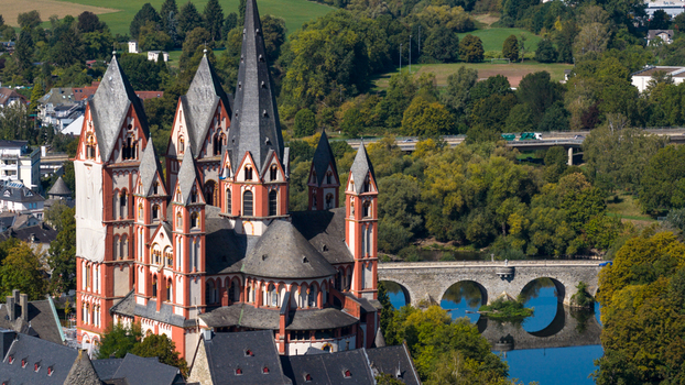 Aerial view of Limburg Cathedral with its distinctive red and white towers surrounded by lush green trees and the Lahn River with its stone bridge in Limburg an der Lahn Hessen Germany. Aerial view of Limburg Cathedral with its distinctive red and white towers surrounded by lush green trees and the Lahn River with its stone bridge in Limburg an der Lahn Hessen Germany.