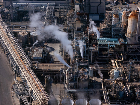 Aerial view of an industrial oil refinery complex with complex piping systems storage tanks and steam rising from cooling towers in Carson California United States.