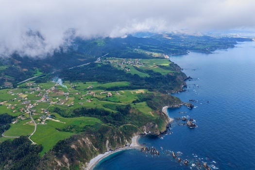 Aerial view of Silence Beach Viewpoint and the rugged coastline with green meadows and small villages under a cloudy sky in Cudillero Asturias Spain.