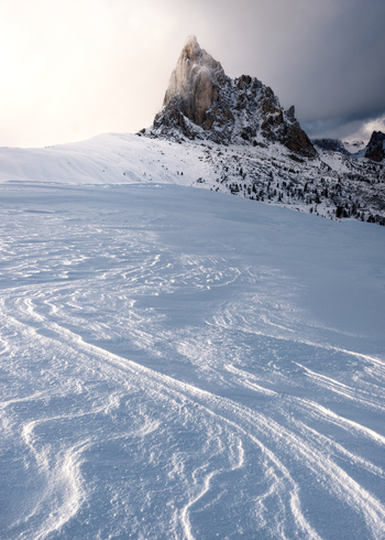 View of the snow covered Dolomites mountain peak rising above a vast wind swept snowfield under a soft winter light Trentino Alto Adige Italy. View of the snow covered Dolomites mountain peak rising above a vast wind swept snowfield under a soft winter light Trentino Alto Adige Italy.