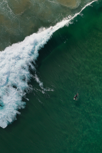 Aerial view of a surfer paddling in the clear turquoise ocean near a breaking wave at Dee Why New South Wales Australia.