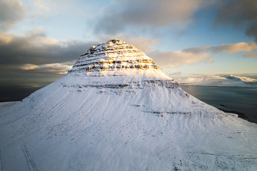 Aerial view of snow clad Kirkjufell mountain under a soft sky its stark white contrasting with the muted blues of the surrounding sea Kirkjufell Iceland.