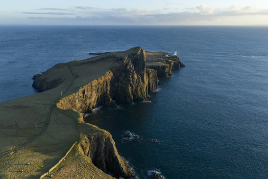 Aerial view of Neist Point Lighthouse perched on dramatic rocky cliffs overlooking the deep blue Atlantic Ocean during golden hour Isle of Skye Scotland United Kingdom. Aerial view of Neist Point Lighthouse perched on dramatic rocky cliffs overlooking the deep blue Atlantic Ocean during golden hour Isle of Skye Scotland United Kingdom.