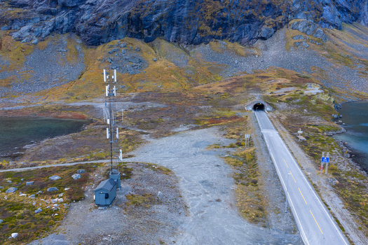 Aerial view of the Oppljostunell tunnel entrance and a nearby telecommunications tower situated along a mountain road beside a lake in Skjak Innlandet Norway. Aerial view of the Oppljostunell tunnel entrance and a nearby telecommunications tower situated along a mountain road beside a lake in Skjak Innlandet Norway.