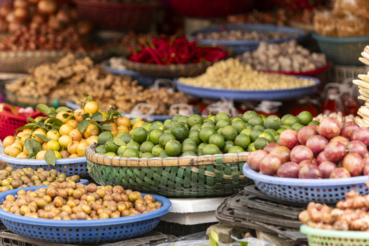 View of a vibrant street market stall filled with baskets of fresh tropical fruits including limes kumquats and passion fruit in Hanoi Ha Noi Vietnam.
