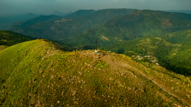 Aerial view of Mt. Gemi with a cross on the summit surrounded by lush green hills rocky terrain and distant mountains in Amedzofe Volta Region Ghana. Aerial view of Mt. Gemi with a cross on the summit surrounded by lush green hills rocky terrain and distant mountains in Amedzofe Volta Region Ghana.