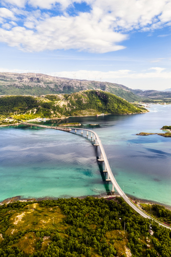 Aerial view of the Sommaroy bridge connecting islands over turquoise waters with green hills and a blue sky in Sommaroy Troms Norway. Aerial view of the Sommaroy bridge connecting islands over turquoise waters with green hills and a blue sky in Sommaroy Troms Norway.