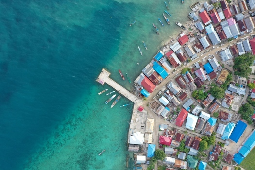 Aerial view of Pulau Maginti featuring a pier in turquoise waters with small boats and a dense coastal village with colorful rooftops Maginti South East Sulawesi Indonesia.