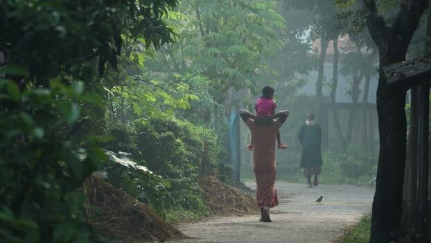 View of a man carrying a child on a misty path in Bogura Bangladesh.