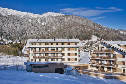 View of bright buildings with dark balconies surrounded by snow and a forest covered mountain under a clear blue sky Donovaly Banska Bystrica Region Slovakia. View of bright buildings with dark balconies surrounded by snow and a forest covered mountain under a clear blue sky Donovaly Banska Bystrica Region Slovakia.