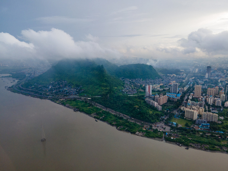 Aerial view of lush green hills and urban landscape featuring dense residential buildings a winding road and the expansive Thane Creek under a cloudy sky in Thane Maharashtra India. Aerial view of lush green hills and urban landscape featuring dense residential buildings a winding road and the expansive Thane Creek under a cloudy sky in Thane Maharashtra India.