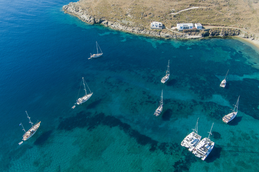 Greece 21 September 2026 Aerial view of sailboats and catamarans anchored in a clear blue bay with a rocky coastline and white buildings. Greece 21 September 2026 Aerial view of sailboats and catamarans anchored in a clear blue bay with a rocky coastline and white buildings.