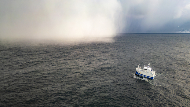 Aerial view of a small fishing boat navigating through dark choppy waters under a dramatic misty sky near the coast in Reine Nordland Norway.
