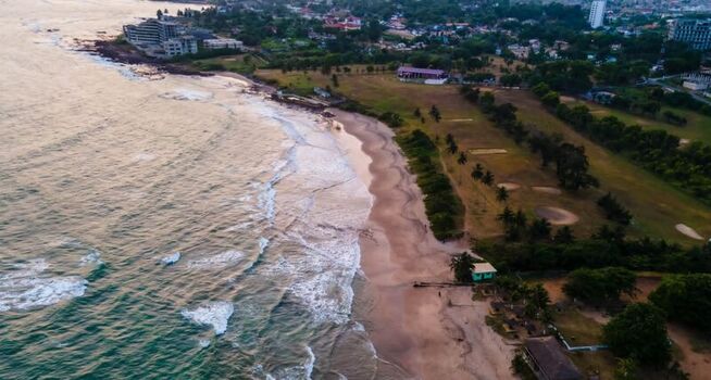 Aerial view of a sandy beach with gentle ocean waves coastal vegetation and nearby resort buildings along the shoreline in Ghana. Aerial view of a sandy beach with gentle ocean waves coastal vegetation and nearby resort buildings along the shoreline in Ghana.