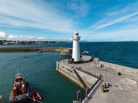 Aerial view of Donaghadee Harbour featuring the white lighthouse on the stone pier with a lifeboat in the blue water under a clear sky in Donaghadee Northern Ireland United Kingdom. Aerial view of Donaghadee Harbour featuring the white lighthouse on the stone pier with a lifeboat in the blue water under a clear sky in Donaghadee Northern Ireland United Kingdom.