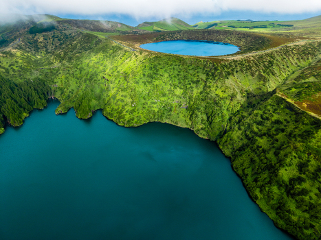 Aerial view of the deep blue waters meeting the lush green cliffs surrounding Lake Comprida a volcanic crater lake Flores Azores Portugal.