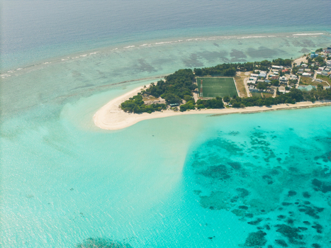 Aerial view of turquoise waters swirl around a pristine beach contrasting with the lush greenery and compact buildings Vashafaru Island Thiladhummathi Atoll Maldives.