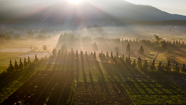Aerial view of Dieng Plateau featuring ancient temples surrounded by misty agricultural fields and rows of cypress trees under a bright sun in Kecamatan Batur Jawa Tengah Indonesia. Aerial view of Dieng Plateau featuring ancient temples surrounded by misty agricultural fields and rows of cypress trees under a bright sun in Kecamatan Batur Jawa Tengah Indonesia.