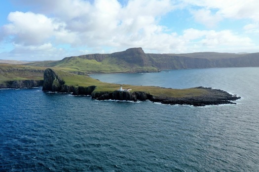 Aerial view of Neist Point Lighthouse situated on a dramatic cliff edge surrounded by the deep blue waters of the Atlantic Ocean on the Isle of Skye Scotland United Kingdom.