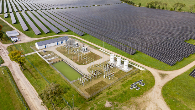 Aerial view of a large solar farm with rows of photovoltaic panels and an electrical substation in Poland.