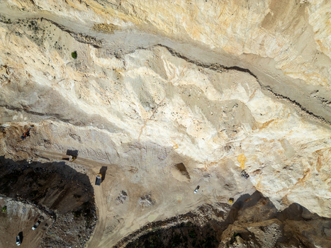 Aerial view of a large open pit quarry with heavy machinery excavators and trucks working on the rocky terrain in Teulada Valencian Community Spain.
