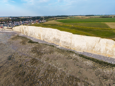 Aerial view of the Beach of the Bois de Cise with its dramatic white chalk cliffs rocky shoreline at low tide and lush green fields overlooking the town of Ault Hauts de France France.