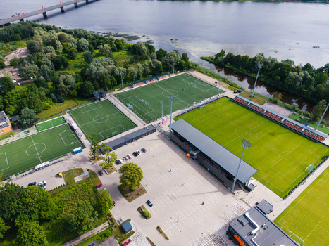 Riga Latvia 05 July 2026 Aerial view of LNK Sporta Parks featuring multiple artificial turf football pitches a parking lot and surrounding trees near the river. Riga Latvia 05 July 2026 Aerial view of LNK Sporta Parks featuring multiple artificial turf football pitches a parking lot and surrounding trees near the river.