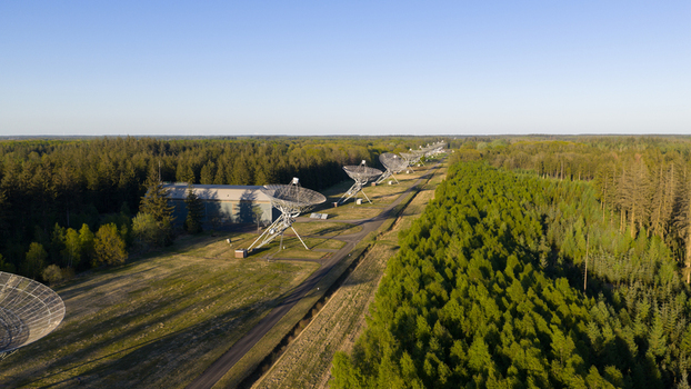Aerial view of the Westerbork Synthesis Radio Telescope dishes lined up through a dense green forest under a clear blue sky in Zwiggelte Drenthe Netherlands. Aerial view of the Westerbork Synthesis Radio Telescope dishes lined up through a dense green forest under a clear blue sky in Zwiggelte Drenthe Netherlands.