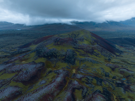 Aerial view of a vibrant moss covered volcanic landscape where shades of green intertwine with rusty reds and dark greys under a brooding sky Snæfellsnes Eyja og Miklaholtshreppur Iceland. Aerial view of a vibrant moss covered volcanic landscape where shades of green intertwine with rusty reds and dark greys under a brooding sky Snæfellsnes Eyja og Miklaholtshreppur Iceland.