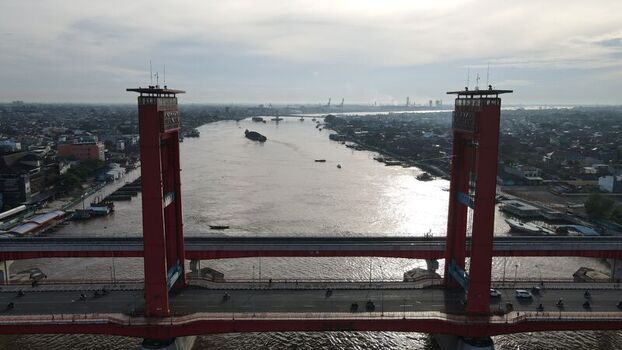 Aerial view of the iconic red Ampera Bridge spanning the Musi River with traffic flowing across and boats navigating the water in Palembang Sumatera Selatan Indonesia. Aerial view of the iconic red Ampera Bridge spanning the Musi River with traffic flowing across and boats navigating the water in Palembang Sumatera Selatan Indonesia.