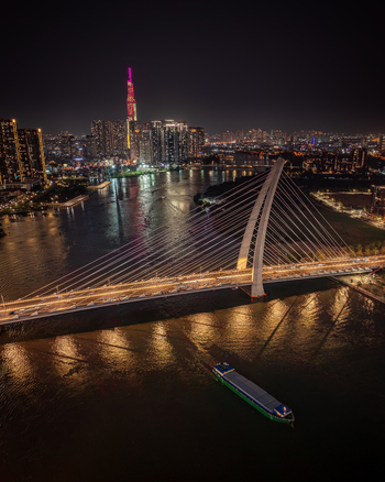 Aerial view of Ba Son Bridge and Landmark 81 skyscraper illuminated at night over the Saigon River in Vietnam. Aerial view of Ba Son Bridge and Landmark 81 skyscraper illuminated at night over the Saigon River in Vietnam.