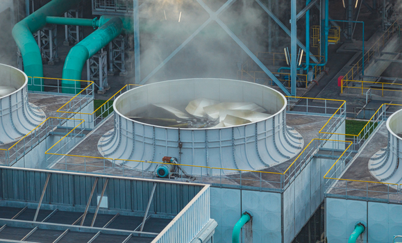 Aerial view of an operating industrial cooling tower with a rotating fan steam and large water pipelines at a manufacturing facility in Brescia Lombardy Italy.