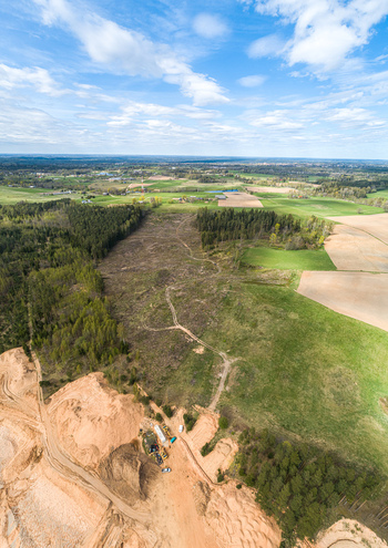 Aerial view of a sand and gravel quarry surrounded by green fields dense forests and dirt tracks under a bright blue sky in Latvia. Aerial view of a sand and gravel quarry surrounded by green fields dense forests and dirt tracks under a bright blue sky in Latvia.
