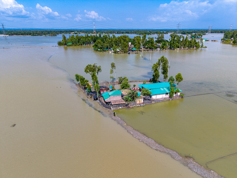 Aerial view of houses on small islands surrounded by floodwaters with lush green trees and power lines in the distance in Banshkhali Upazila Chittagong Division Bangladesh. Aerial view of houses on small islands surrounded by floodwaters with lush green trees and power lines in the distance in Banshkhali Upazila Chittagong Division Bangladesh.