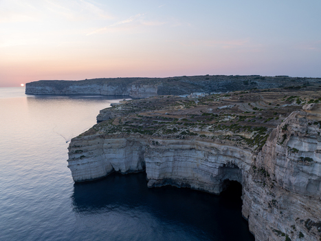 Aerial view of rugged cliffs meet the tranquil blue sea under the soft glow of the setting sun at Sanap Cliffs Munxar Gozo Malta. Aerial view of rugged cliffs meet the tranquil blue sea under the soft glow of the setting sun at Sanap Cliffs Munxar Gozo Malta.