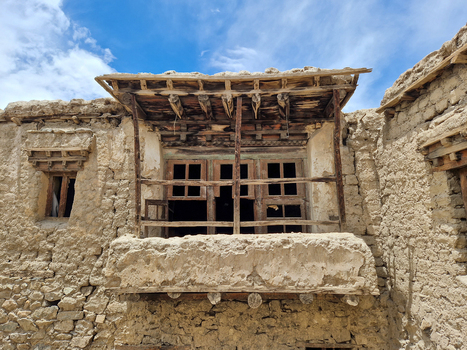 View of a traditional mud brick building with a weathered wooden balcony and rustic architectural details under a clear blue sky in Leh Ladakh India.