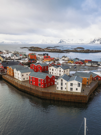 Aerial view of vibrant red and white houses cluster along the harbor s edge contrasting against the cold sea and snow dusted mountains Henningsv&aelig;r Nordland Norway.