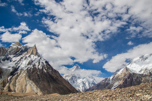 View of the K2 mountain peak surrounded by snow capped ridges and rocky terrain under a cloudy blue sky Skardu Gilgit Pakistan.