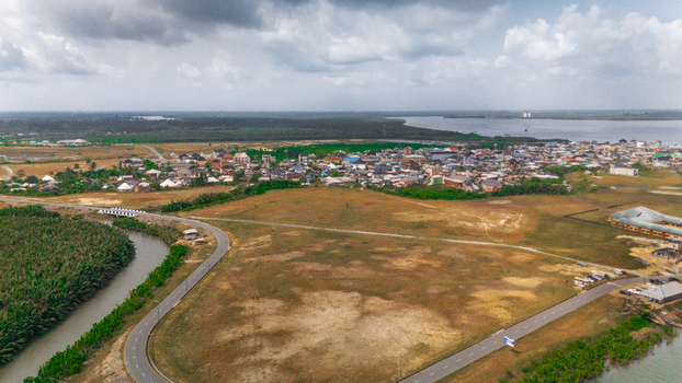 Aerial view of a coastal town nestled between a winding river and lush greenery featuring residential buildings paved roads and a cloudy sky in Minima Rivers Nigeria.