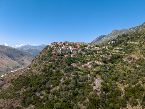 Aerial view of stone houses of a traditional hillside village nestled among lush green vegetation and olive groves under a clear blue sky in Qeparo Fshat Vlore County Albania. Aerial view of stone houses of a traditional hillside village nestled among lush green vegetation and olive groves under a clear blue sky in Qeparo Fshat Vlore County Albania.