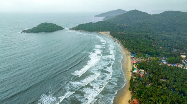 Aerial view of Palolem Beach with its crescent shaped coastline lush green hills tropical palm trees and gentle waves rolling onto the sandy shore in Canacona Goa India.