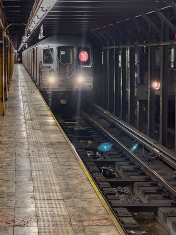 View of a New York City Subway train with headlights on approaching a station platform along the tracks New York New York United States. View of a New York City Subway train with headlights on approaching a station platform along the tracks New York New York United States.