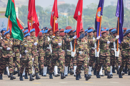 Dhaka Bangladesh 25 March 2026 View of uniformed soldiers marching in formation their camouflage blending against the backdrop of vibrant national flags.